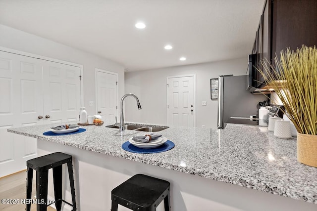 kitchen with light stone counters, stainless steel refrigerator, a breakfast bar area, and sink