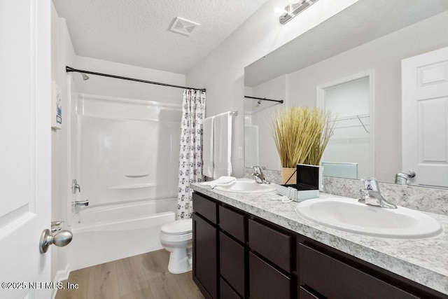 full bathroom featuring hardwood / wood-style floors, vanity, toilet, shower / bath combo with shower curtain, and a textured ceiling