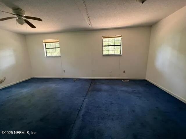 unfurnished room with ceiling fan, a textured ceiling, and dark colored carpet