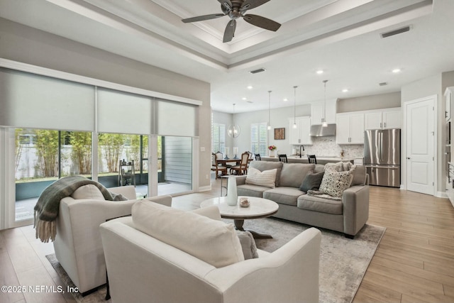 living room with crown molding, light hardwood / wood-style flooring, a healthy amount of sunlight, and ceiling fan with notable chandelier