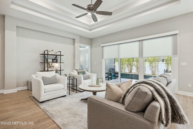 living room with a tray ceiling, light hardwood / wood-style flooring, ceiling fan, and ornamental molding