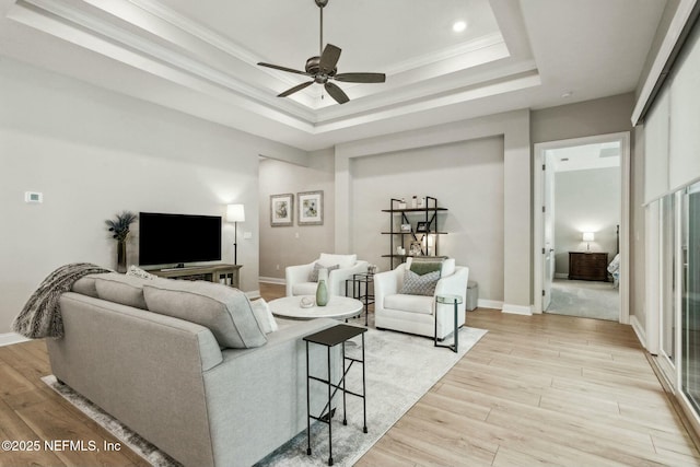 living room with ceiling fan, a raised ceiling, ornamental molding, and light hardwood / wood-style flooring