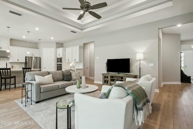 living room featuring ceiling fan, light hardwood / wood-style flooring, crown molding, and a tray ceiling