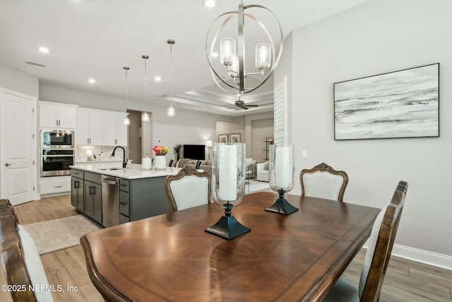 dining space featuring ceiling fan with notable chandelier, light hardwood / wood-style floors, a raised ceiling, and sink