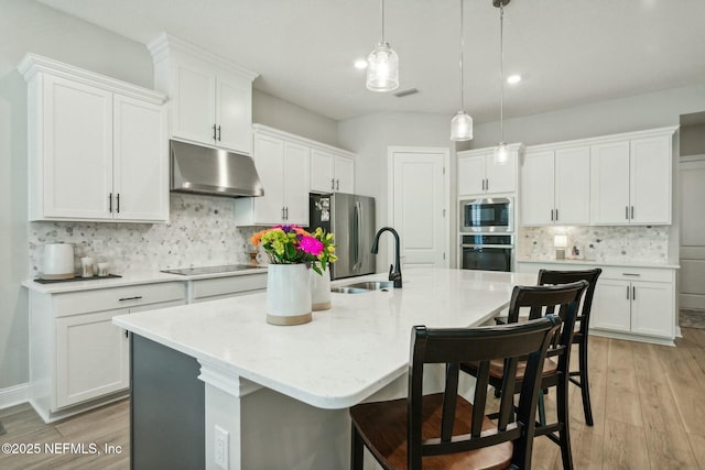 kitchen featuring hanging light fixtures, appliances with stainless steel finishes, white cabinetry, and a kitchen island with sink