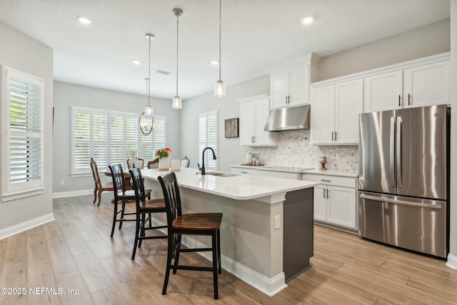 kitchen with hanging light fixtures, stainless steel fridge, white cabinetry, and a kitchen island with sink