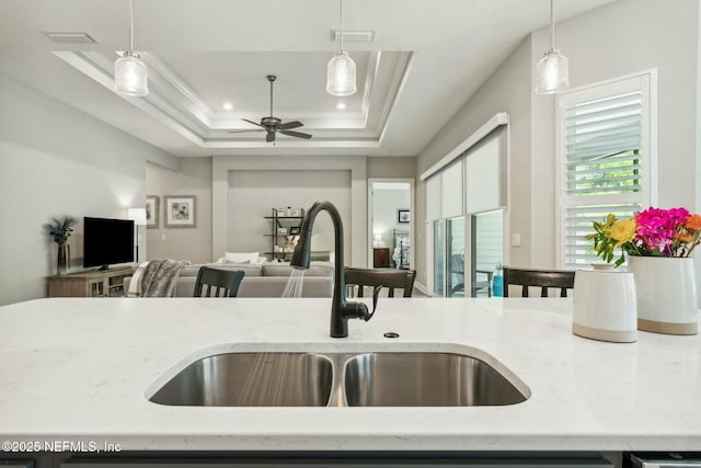 kitchen with a raised ceiling, sink, hanging light fixtures, crown molding, and light stone counters