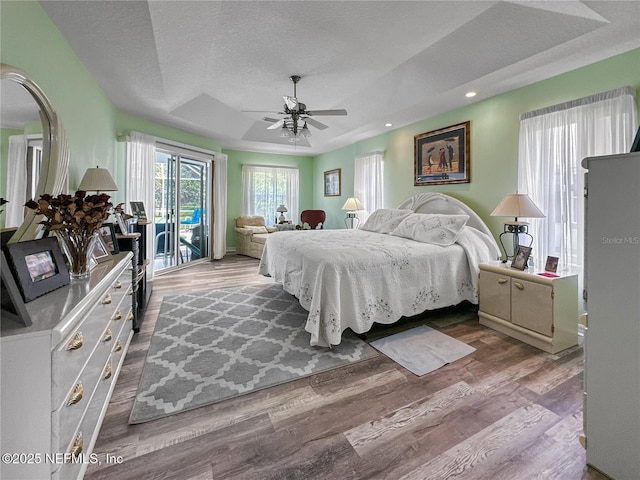 bedroom with access to exterior, a textured ceiling, a raised ceiling, ceiling fan, and wood-type flooring