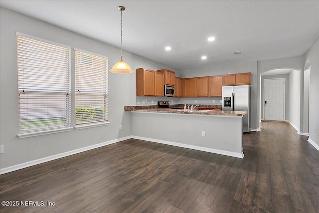 kitchen with stainless steel appliances, kitchen peninsula, dark wood-type flooring, and hanging light fixtures