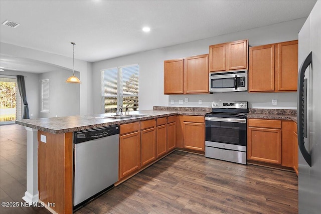 kitchen with kitchen peninsula, appliances with stainless steel finishes, sink, dark hardwood / wood-style floors, and hanging light fixtures