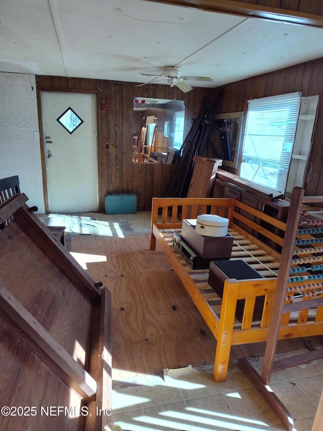 misc room featuring light tile patterned floors, wooden walls, and ceiling fan