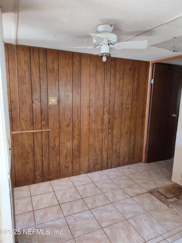 empty room with light tile patterned floors, ceiling fan, and wood walls