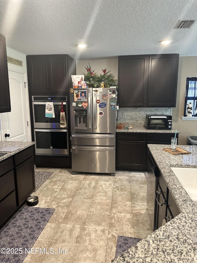 kitchen with light stone counters, sink, stainless steel appliances, and a textured ceiling