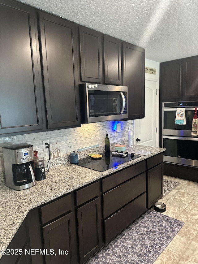 kitchen featuring light stone countertops, backsplash, a textured ceiling, dark brown cabinetry, and stainless steel appliances