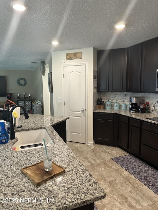 kitchen with tasteful backsplash, light stone counters, sink, and a textured ceiling