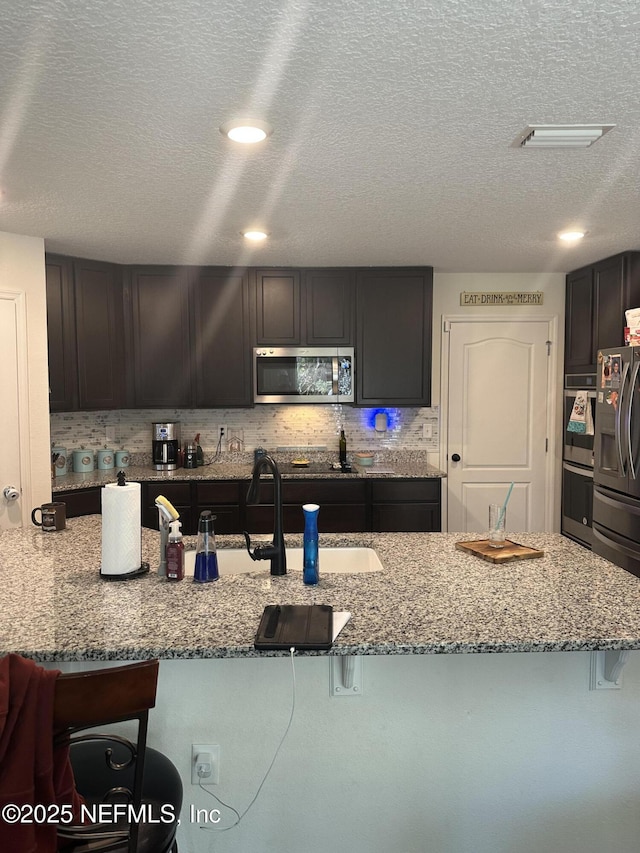 kitchen with light stone countertops, appliances with stainless steel finishes, a textured ceiling, and a kitchen breakfast bar