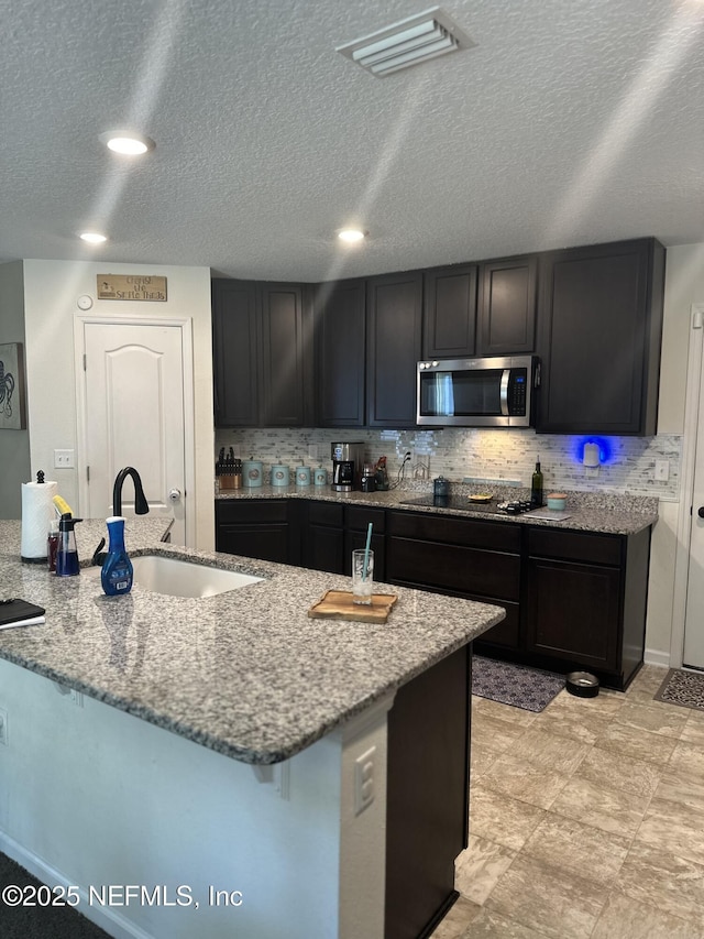 kitchen with decorative backsplash, light stone counters, black electric cooktop, and sink