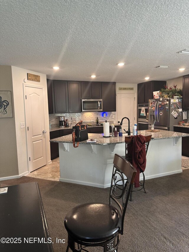 kitchen featuring a breakfast bar, appliances with stainless steel finishes, light stone counters, and an island with sink