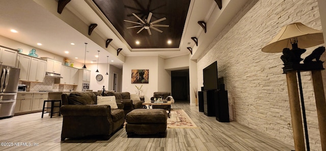 living room with light hardwood / wood-style floors, ceiling fan, and a tray ceiling