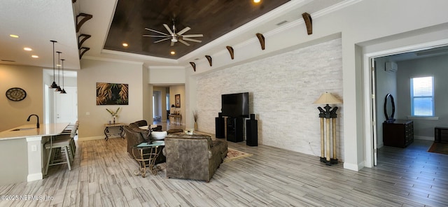 living room featuring light wood-type flooring, ornamental molding, a raised ceiling, ceiling fan, and sink