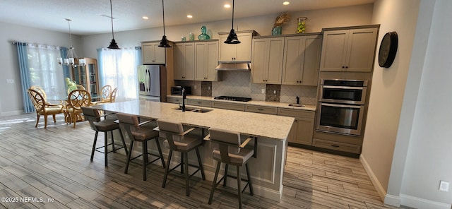 kitchen with a breakfast bar, a center island with sink, hanging light fixtures, light stone counters, and stainless steel appliances