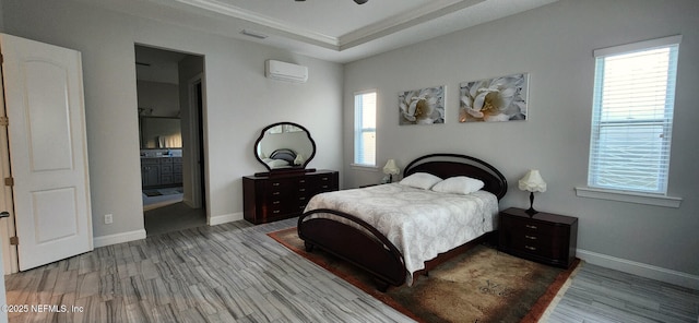 bedroom with hardwood / wood-style floors, ceiling fan, a wall unit AC, and a tray ceiling