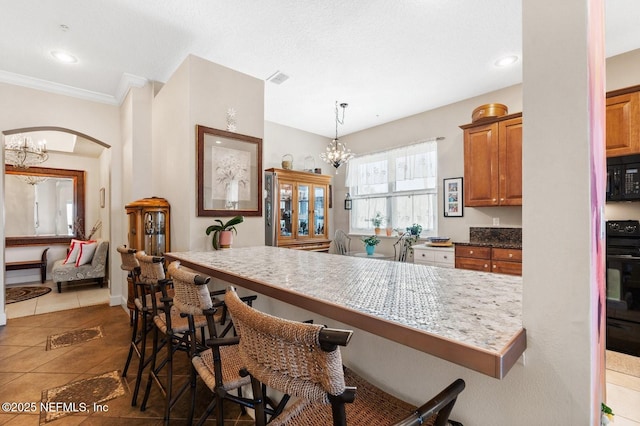 kitchen with a kitchen breakfast bar, black appliances, decorative light fixtures, dark tile patterned flooring, and a notable chandelier