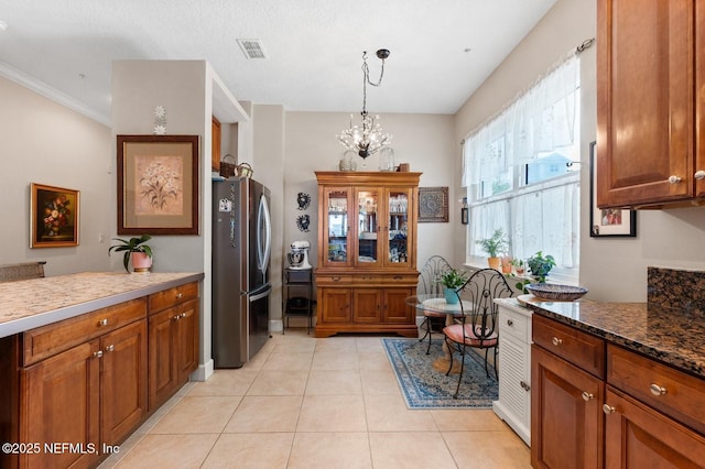 kitchen featuring pendant lighting, stainless steel fridge, a notable chandelier, light tile patterned flooring, and dark stone counters