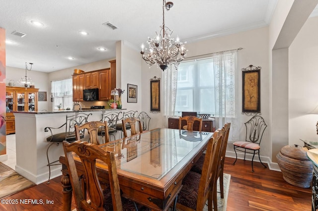 dining area with a textured ceiling, ornamental molding, dark wood-type flooring, and a chandelier