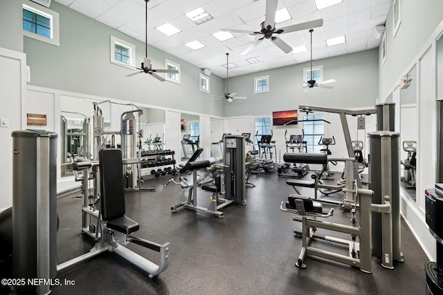 gym with ceiling fan, a towering ceiling, and a drop ceiling