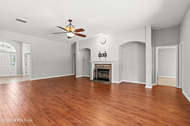 unfurnished living room featuring hardwood / wood-style flooring, ceiling fan, a textured ceiling, and a brick fireplace