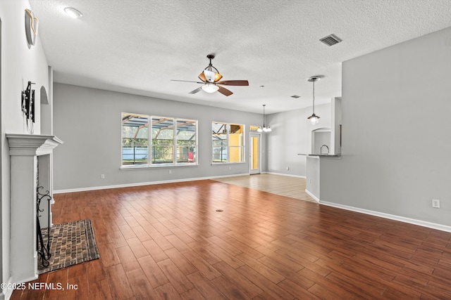 unfurnished living room with a textured ceiling, wood-type flooring, and ceiling fan with notable chandelier