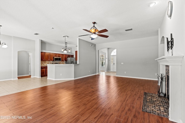 unfurnished living room with a textured ceiling, ceiling fan with notable chandelier, and a tiled fireplace