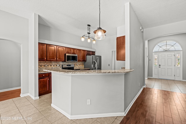 kitchen with light tile patterned floors, tasteful backsplash, decorative light fixtures, light stone counters, and stainless steel appliances