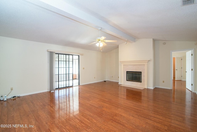 unfurnished living room with a textured ceiling, a premium fireplace, dark hardwood / wood-style floors, lofted ceiling with beams, and ceiling fan