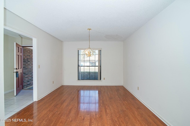 unfurnished dining area featuring an inviting chandelier, a textured ceiling, and light hardwood / wood-style flooring