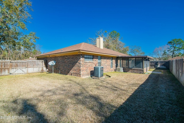 rear view of house with central AC unit, ac unit, a yard, and a sunroom