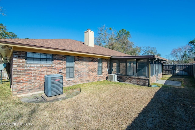 rear view of house with a sunroom, a lawn, and central AC