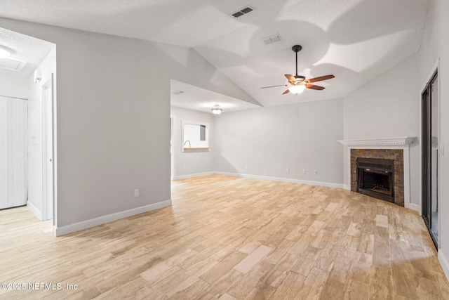 unfurnished living room with vaulted ceiling, ceiling fan, a textured ceiling, light hardwood / wood-style floors, and a tiled fireplace