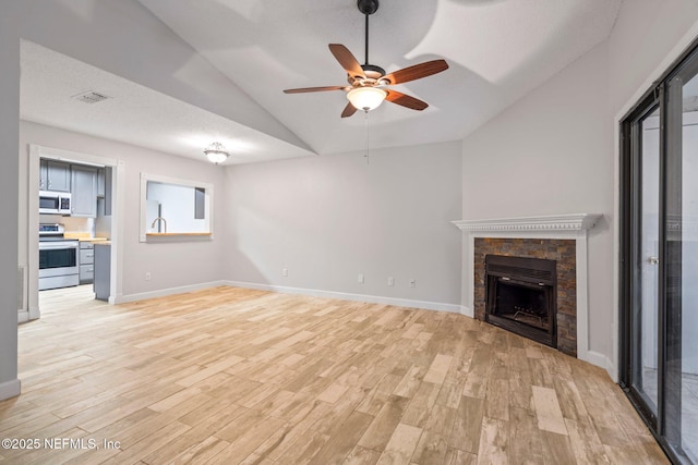 unfurnished living room with light wood-type flooring, a textured ceiling, vaulted ceiling, ceiling fan, and a fireplace