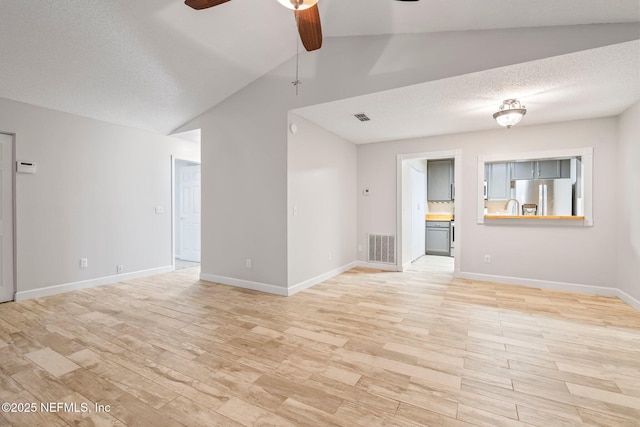 unfurnished living room with a textured ceiling, ceiling fan, light hardwood / wood-style floors, and vaulted ceiling