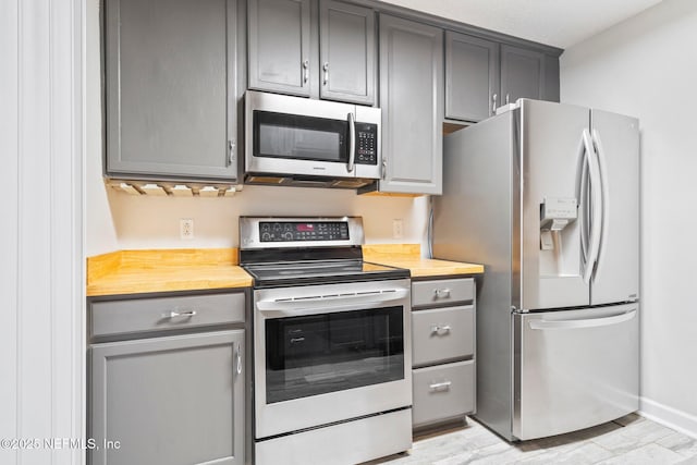 kitchen with gray cabinets, light wood-type flooring, stainless steel appliances, and wooden counters