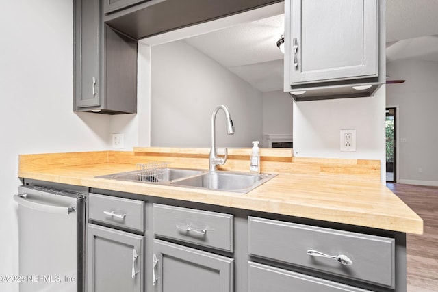 kitchen featuring gray cabinetry, dishwasher, butcher block counters, and sink