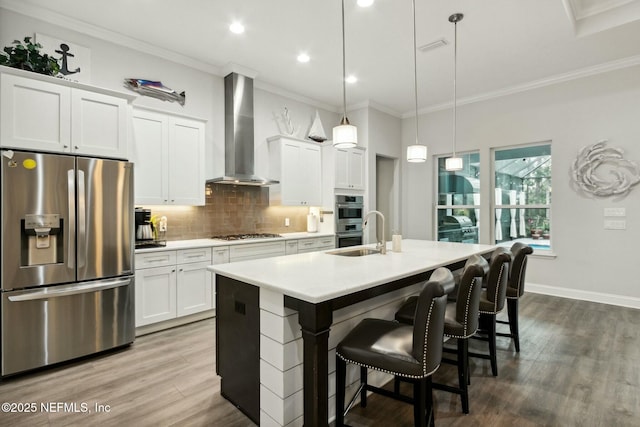 kitchen featuring pendant lighting, a kitchen island with sink, white cabinets, wall chimney range hood, and appliances with stainless steel finishes