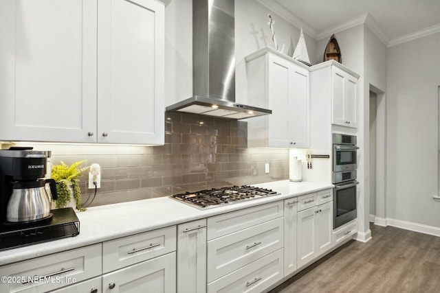 kitchen featuring white cabinetry, wall chimney exhaust hood, tasteful backsplash, wood-type flooring, and appliances with stainless steel finishes