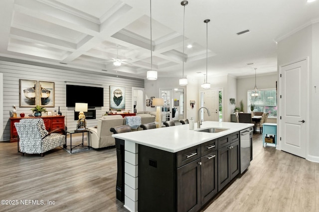 kitchen with coffered ceiling, a kitchen island with sink, wooden walls, sink, and pendant lighting