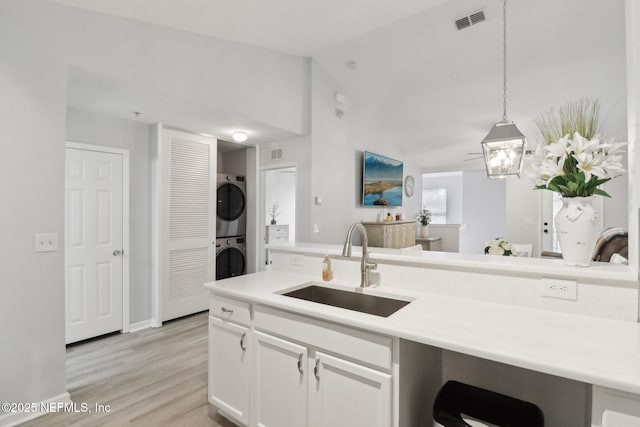 kitchen featuring vaulted ceiling, sink, pendant lighting, stacked washer / dryer, and white cabinetry