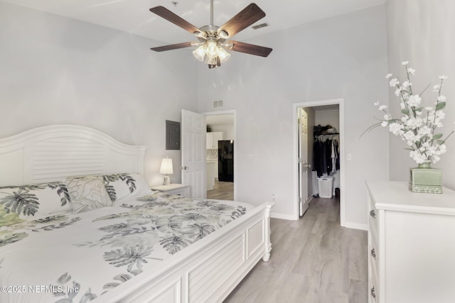 bedroom with a towering ceiling, light wood-type flooring, ceiling fan, a spacious closet, and a closet