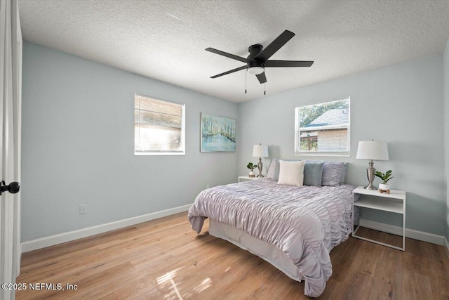 bedroom with ceiling fan, a textured ceiling, multiple windows, and light hardwood / wood-style flooring