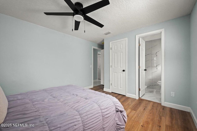 bedroom with a textured ceiling, ceiling fan, connected bathroom, and hardwood / wood-style floors